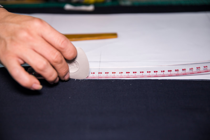 Close up of an artisan tailor marking up the suit pattern onto the fabric with tailor's chalk. 